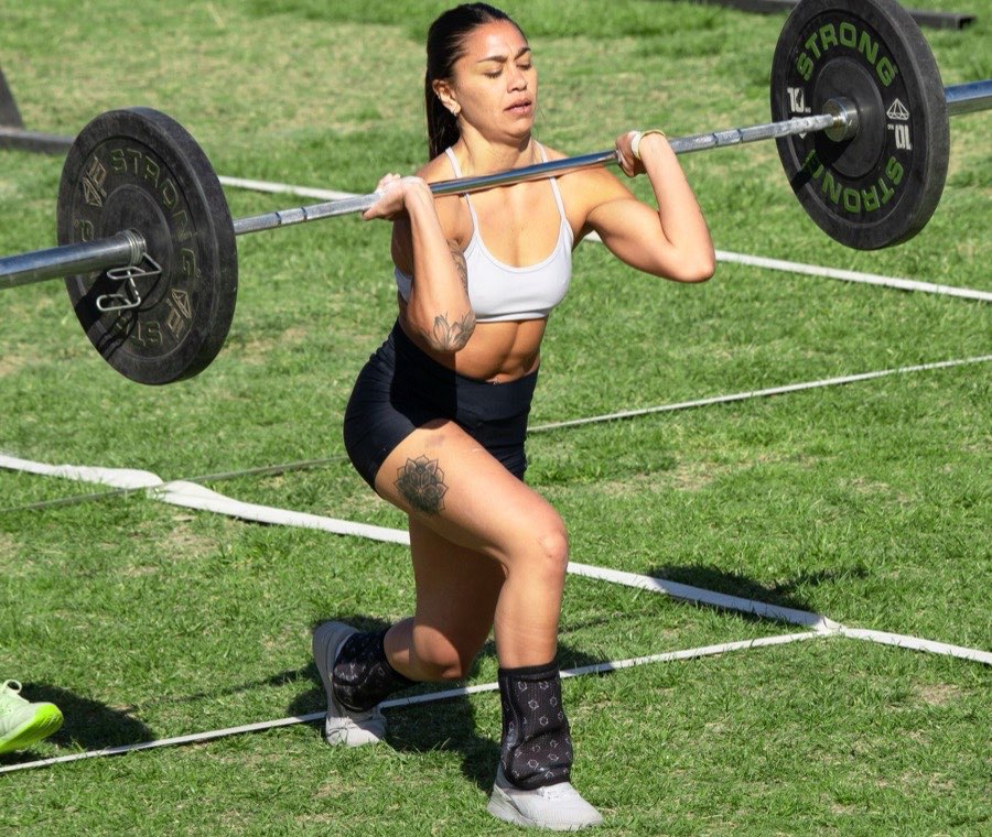 Athlete doing barbell lunges across a marked lane at an outdoor fitness competition