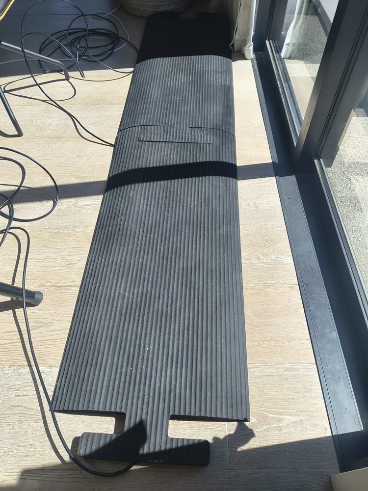 Black ribbed Split Line timing mat laid flat on a timber floor, with its cable running off one end